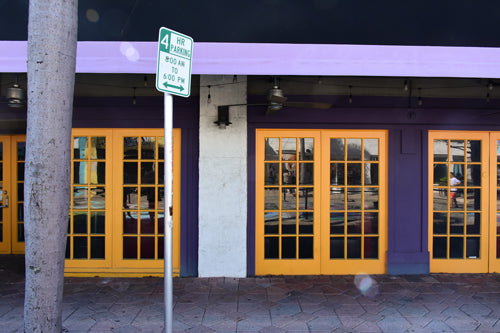 A color photograph featuring a purple building with yellow doors and a street sign that reads '4 Hour Parking'.