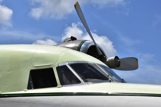 Close-up of a propeller on a light green aircraft against a blue sky with clouds.