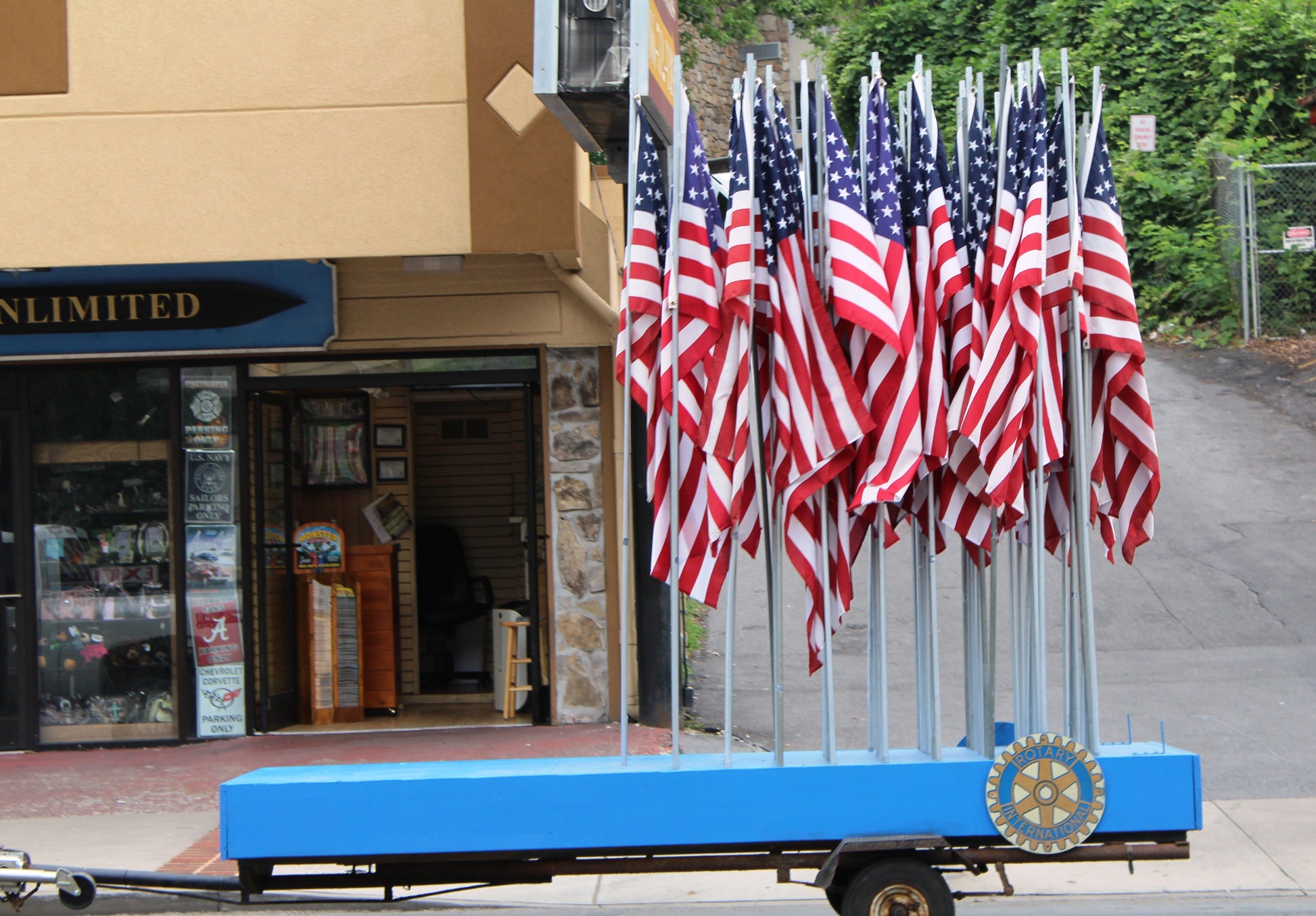 A photograph of American flags displayed on a trailer outside a store, with a small American flag and 'Limited' sign visible in the background.