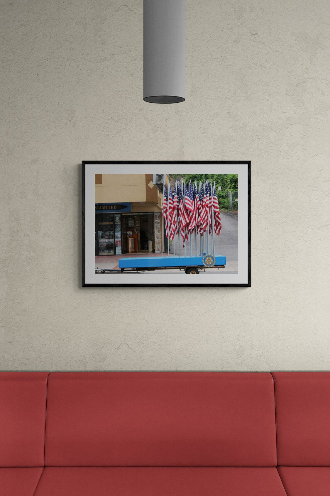 Framed photograph of a truck with American flags parked on a wall above a red couch.