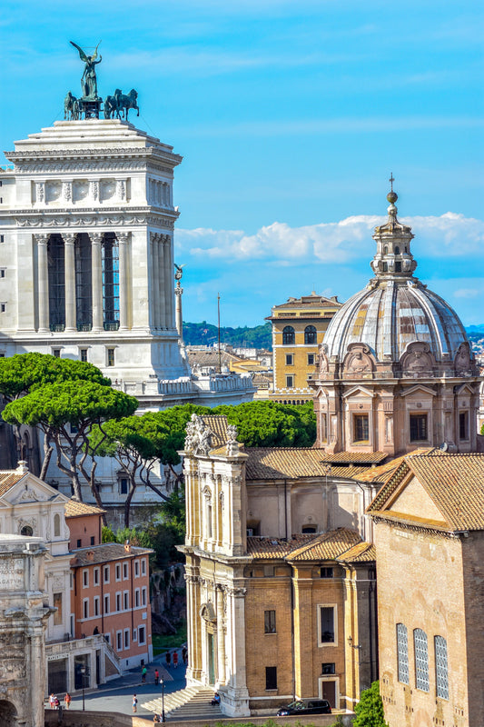 A color photograph depicting the Roman Forum with the Vittoriano Monument and St. Peter's Basilica dome in the background, highlighting architectural details and a clear blue sky. Ancient Rome, Original Photograph by Kim A. Bailey