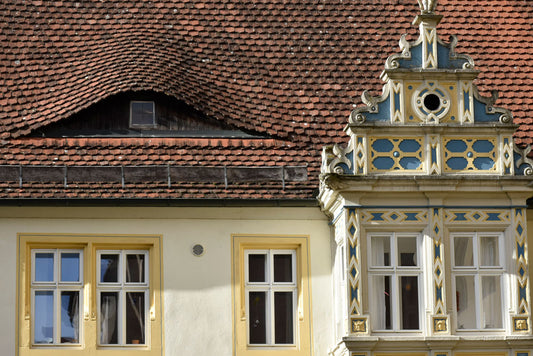 Close-up of the exterior of a Bavarian home in Rothenburg, Germany, showcasing yellow and blue trimmed windows and a vibrant red roof.