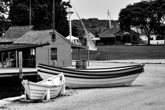A black and white photograph of wooden boats on a beach with rustic shacks in the background, capturing the essence of Mystic, Connecticut.
