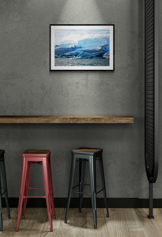 Framed artwork above a wooden ledge with stools below on a gray wall.