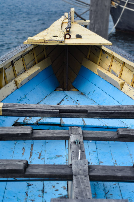 A close-up color photograph of the weathered interior bow of a wooden boat with blue and yellow hues, showcasing the textures and colors of the wood and its maritime journey. Blue and Yellow Boat Original Photograph by Kim A. Bailey