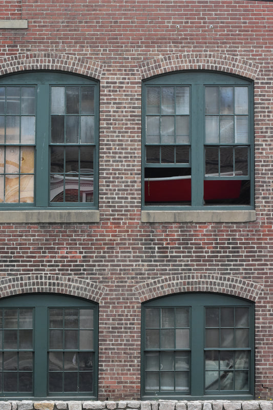 A color photograph of arched windows on a brick wall, with green trim and a reflective glass of a boat museum.
