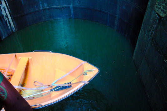 An orange and blue boat navigating through a lock with greenish water visible below. Boat in a Lock - Portugal, Original Photograph by Kim A. Bailey