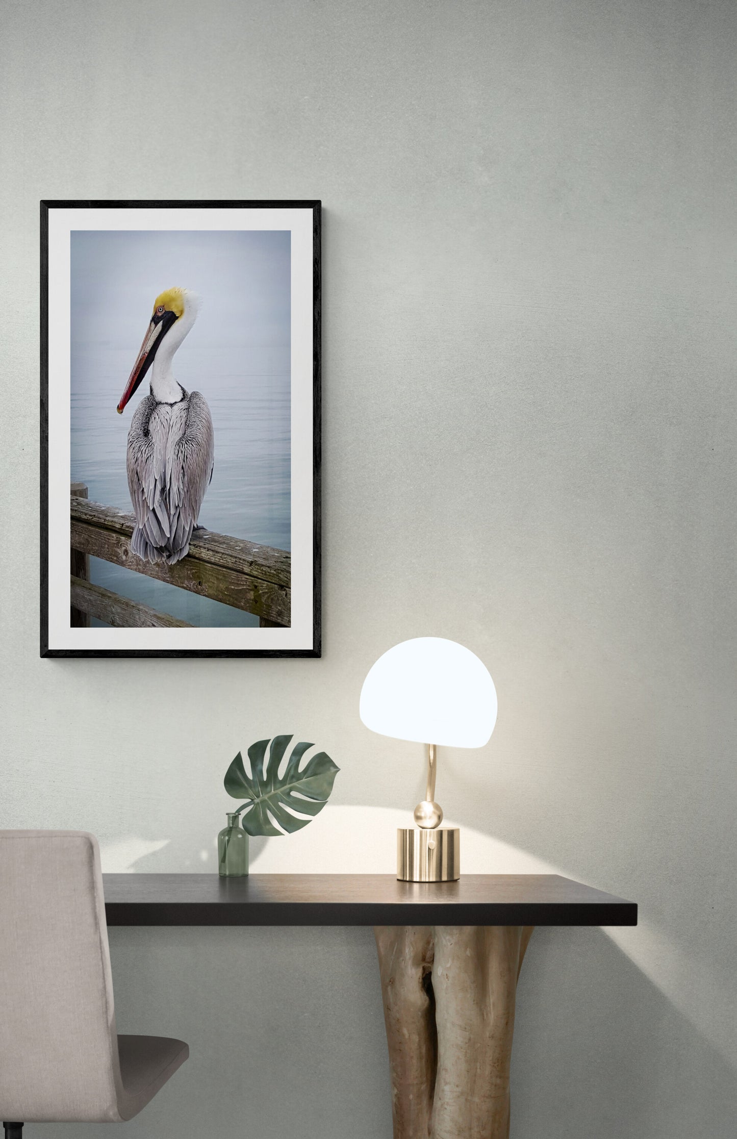 Framed photograph of a pelican by a wall-mounted lamp and chair. Brown Pelican with Yellow Head, Original Photograph by Kim A. Bailey