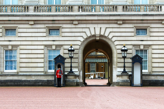 A color photograph of the Buckingham Palace guard standing at his post to the left of the iconic arched entryway, with an empty guard shack on the right. Buckingham Palace Guard, London, England, Original Photograph by Kim A. Bailey