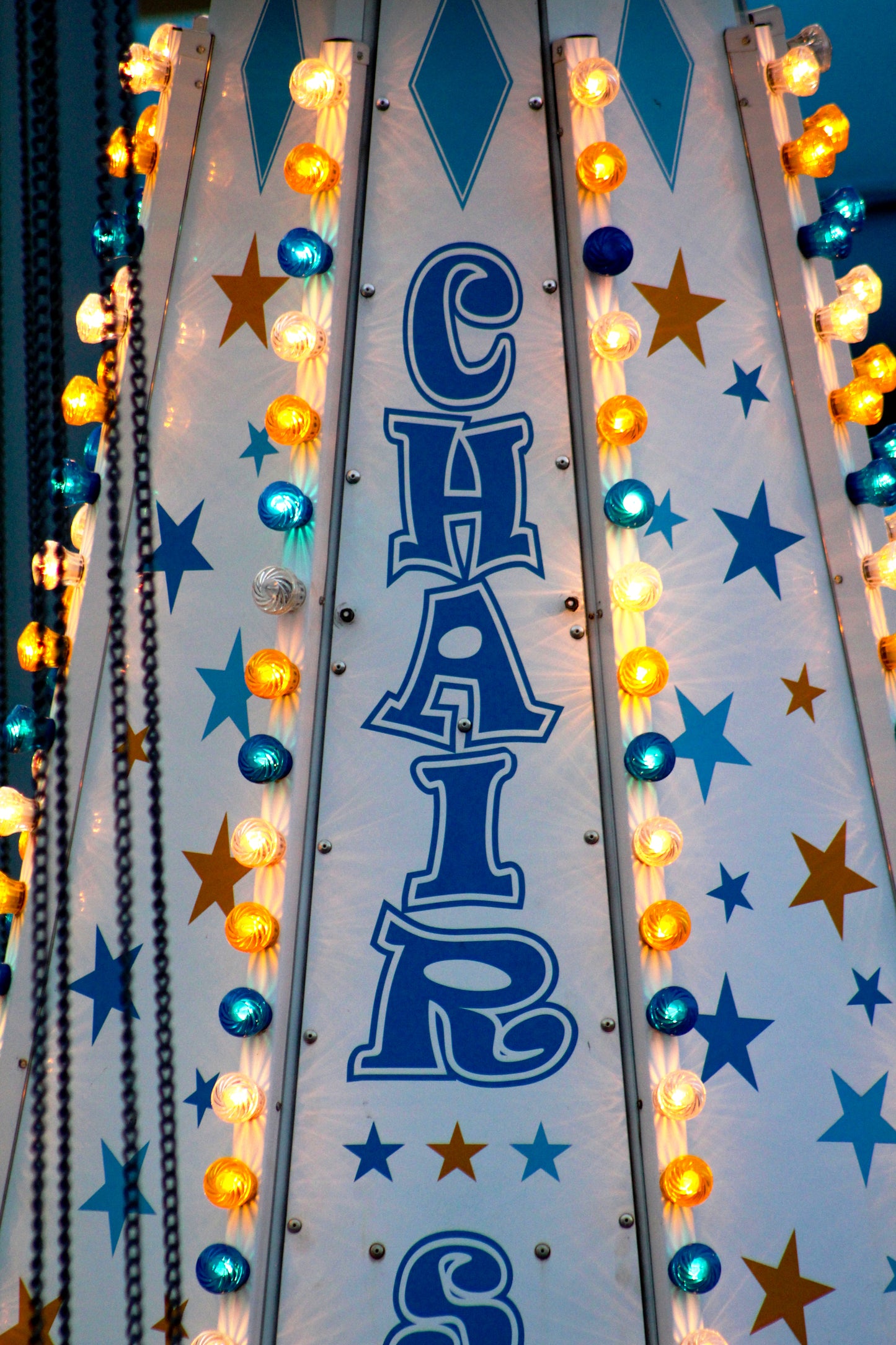 Close-up of a colorful 'CHAIRS' sign for a carnival ride with glowing lights and stars in blue and orange.