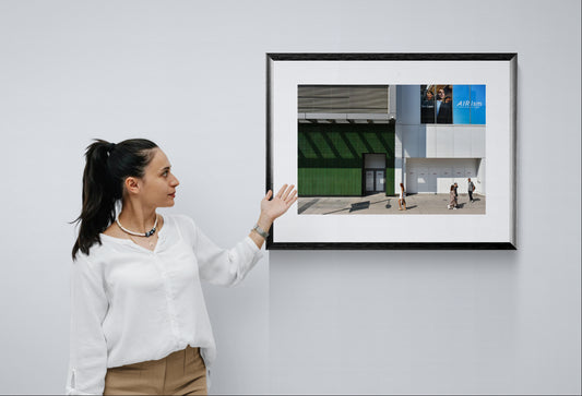 Urban Photograph in big blocks of white, grey, blue, and green colors. People walking through the scene add scale. Framed photograph hanging on a gallery wall.