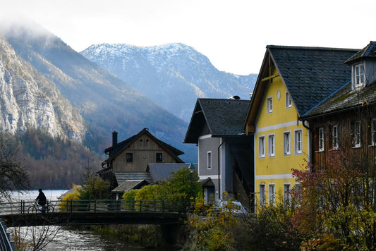 A photograph of a cyclist in Hallstatt, Austria, with a picturesque view of the village surrounded by mountains, featuring colorful houses and a body of water in the foreground.