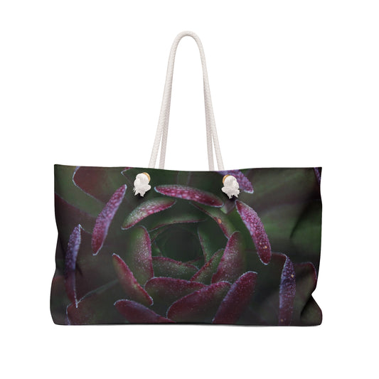 A weekender bag featuring a photograph of a dark succulent plant with purple and green colors on a black background, with rope handles.