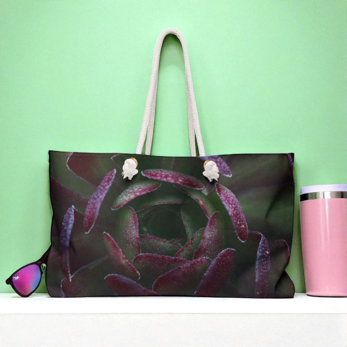 Tote bag with succulent design, pink tumbler, and sunglasses on a green background