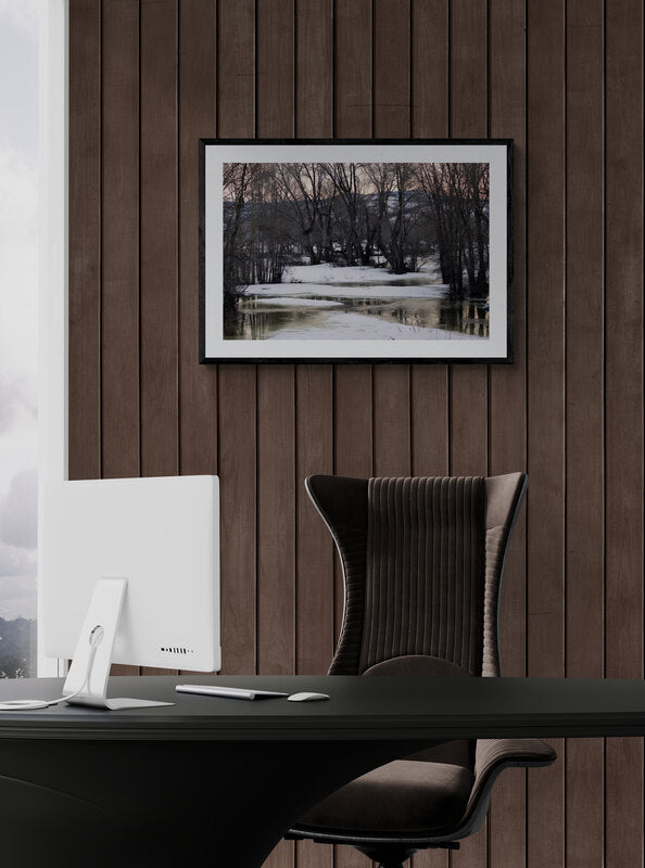 Modern office desk with a computer monitor and chair against a wooden wall with a framed picture. End of Winter, Melting Snow