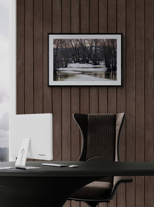Modern office desk with a computer monitor and chair against a wooden wall with a framed picture. End of Winter, Melting Snow