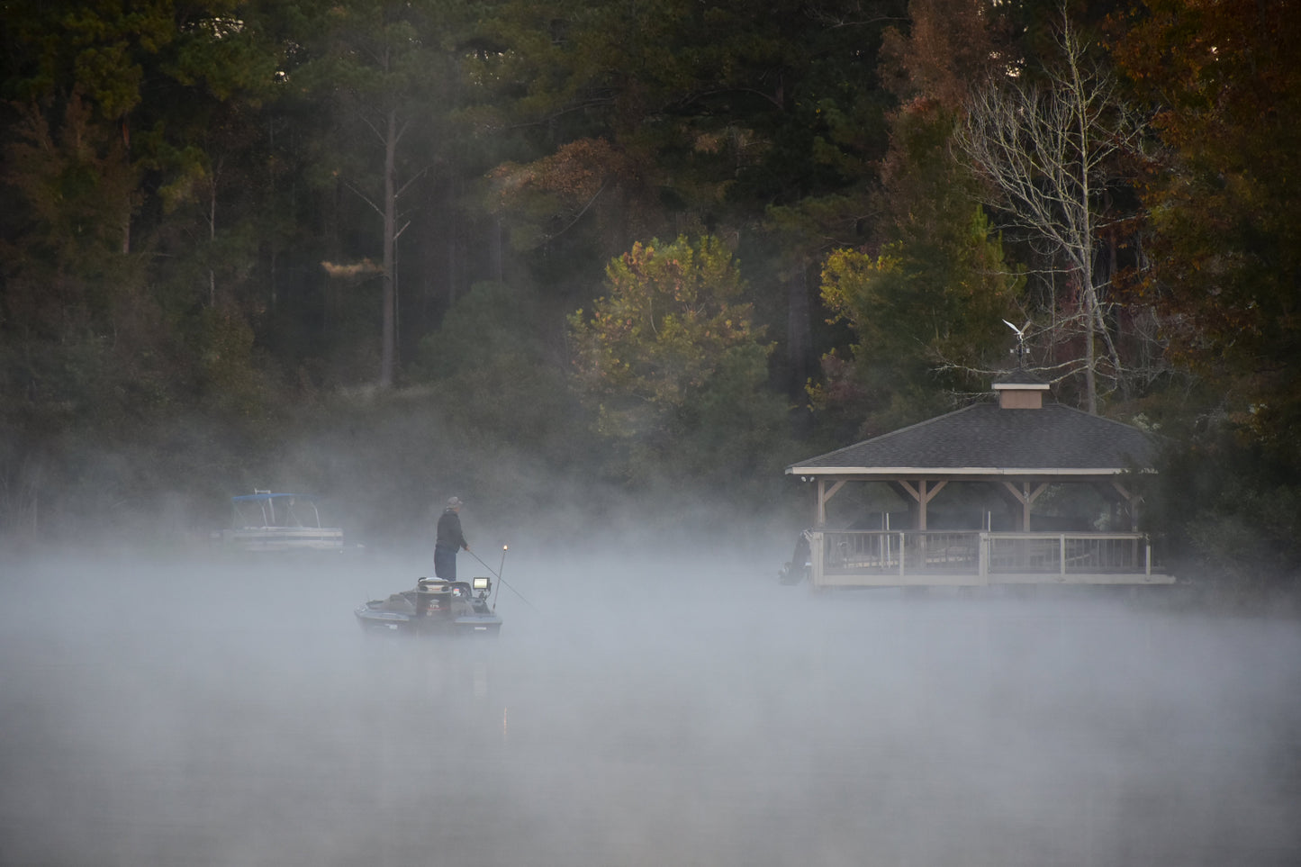 Person on a boat in a foggy lake with a gazebo in the background