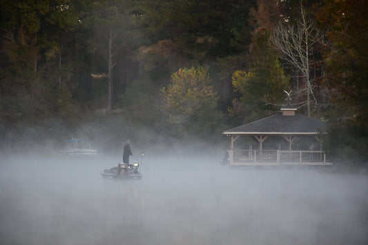 Person on a boat in a foggy lake with a gazebo in the background