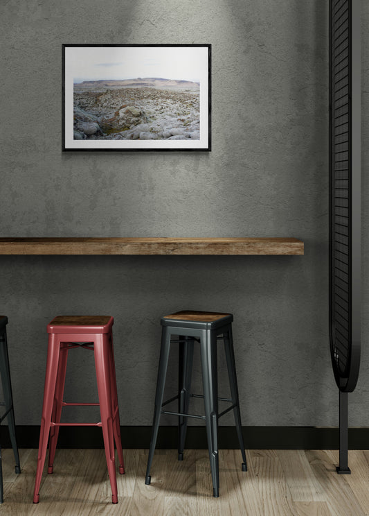 Two bar stools in front of a wall with a framed picture.