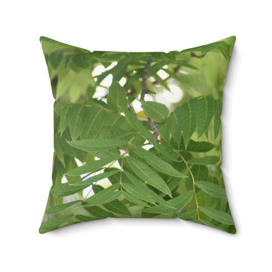 A square-shaped throw pillow with a faux suede cover featuring a vibrant green tree leaf design.