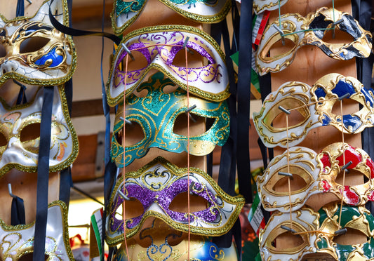A collection of colorful Venetian masks displayed in a market setting, featuring intricate designs and a variety of colors.