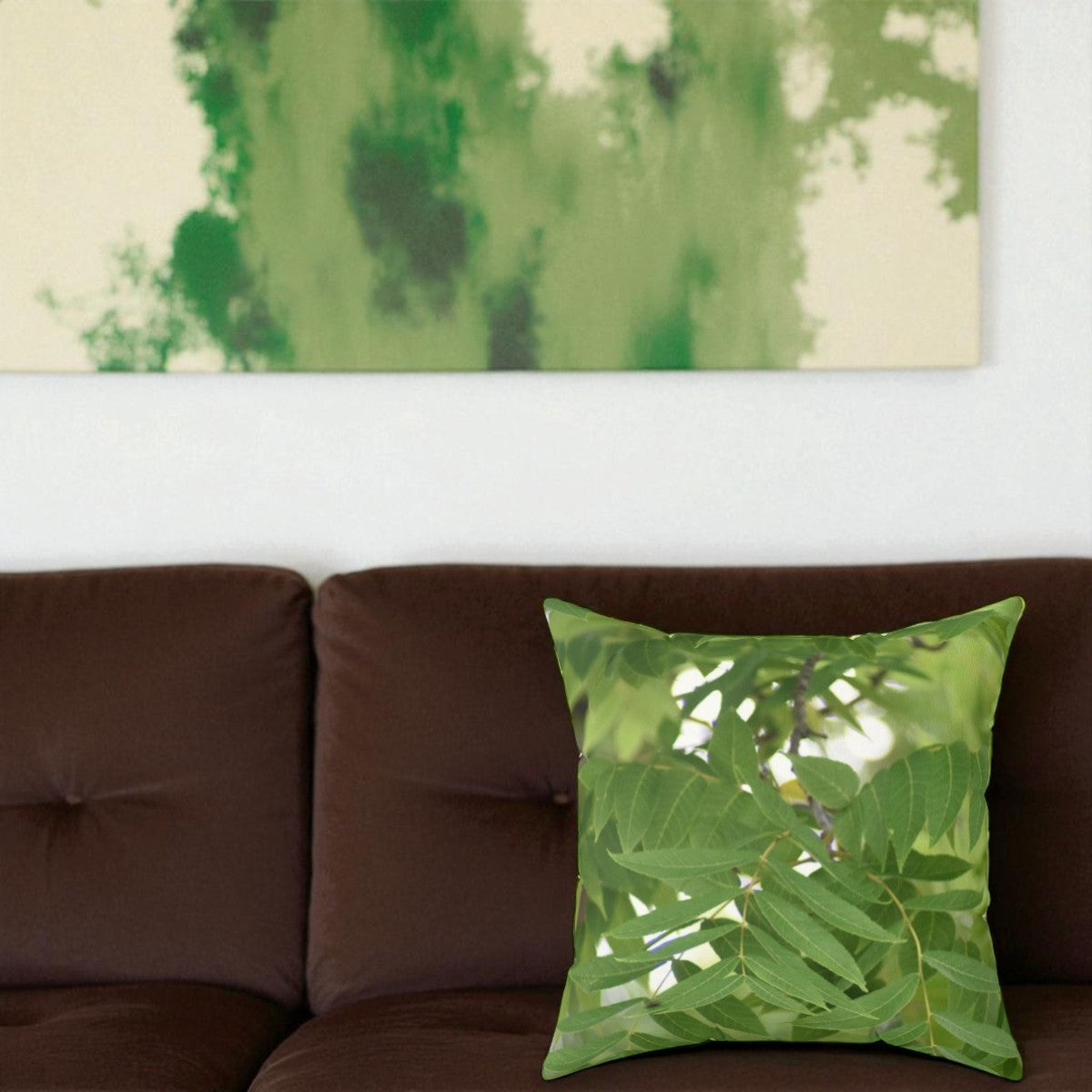 Green leaf-patterned pillow on a brown couch with a abstract green and beige painting in the background.