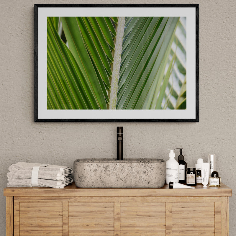 Framed artwork of green leaves above a bathroom counter with towels and toiletries.