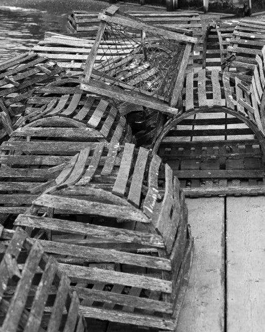 A black and white photograph of old wooden lobster traps arranged neatly on the ground, showcasing their weathered texture. Lobster Traps Original Black and White Photograph by Kim A. Bailey