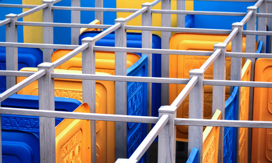 An abstract photograph of a brightly colored outdoor maze with vivid blue and yellow partitions forming geometric paths and playful intersections.