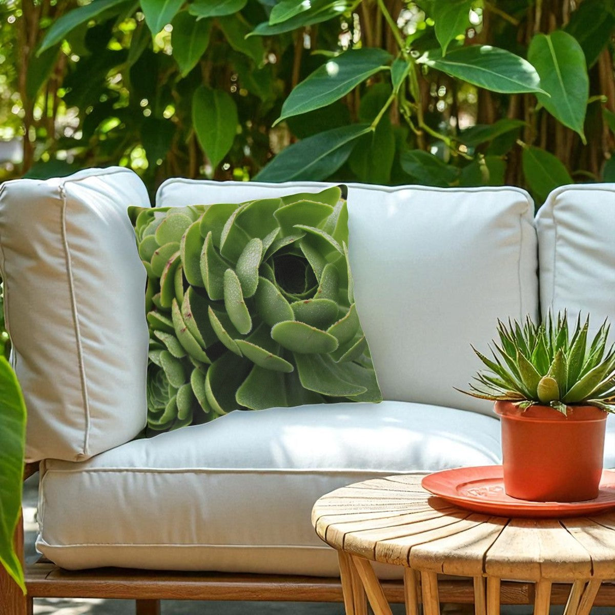 White outdoor sofa with a green pillow and a small potted plant on a wooden table.