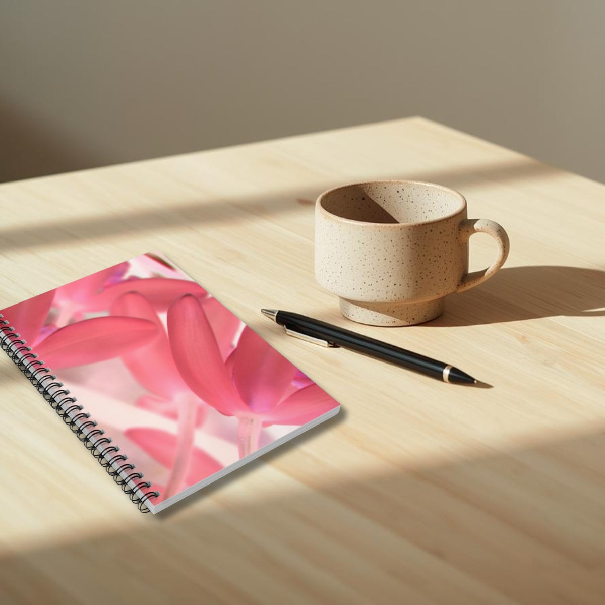 Notebook with pink floral cover, pen, and ceramic mug on a wooden surface