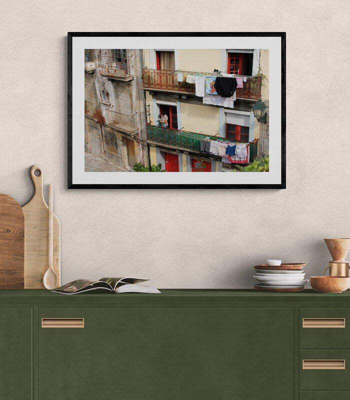 Framed photograph of a street scene with laundry hanging, above a green cabinet. Portuguese Woman Hanging Laundry, Original Photograph by Kim A. Bailey