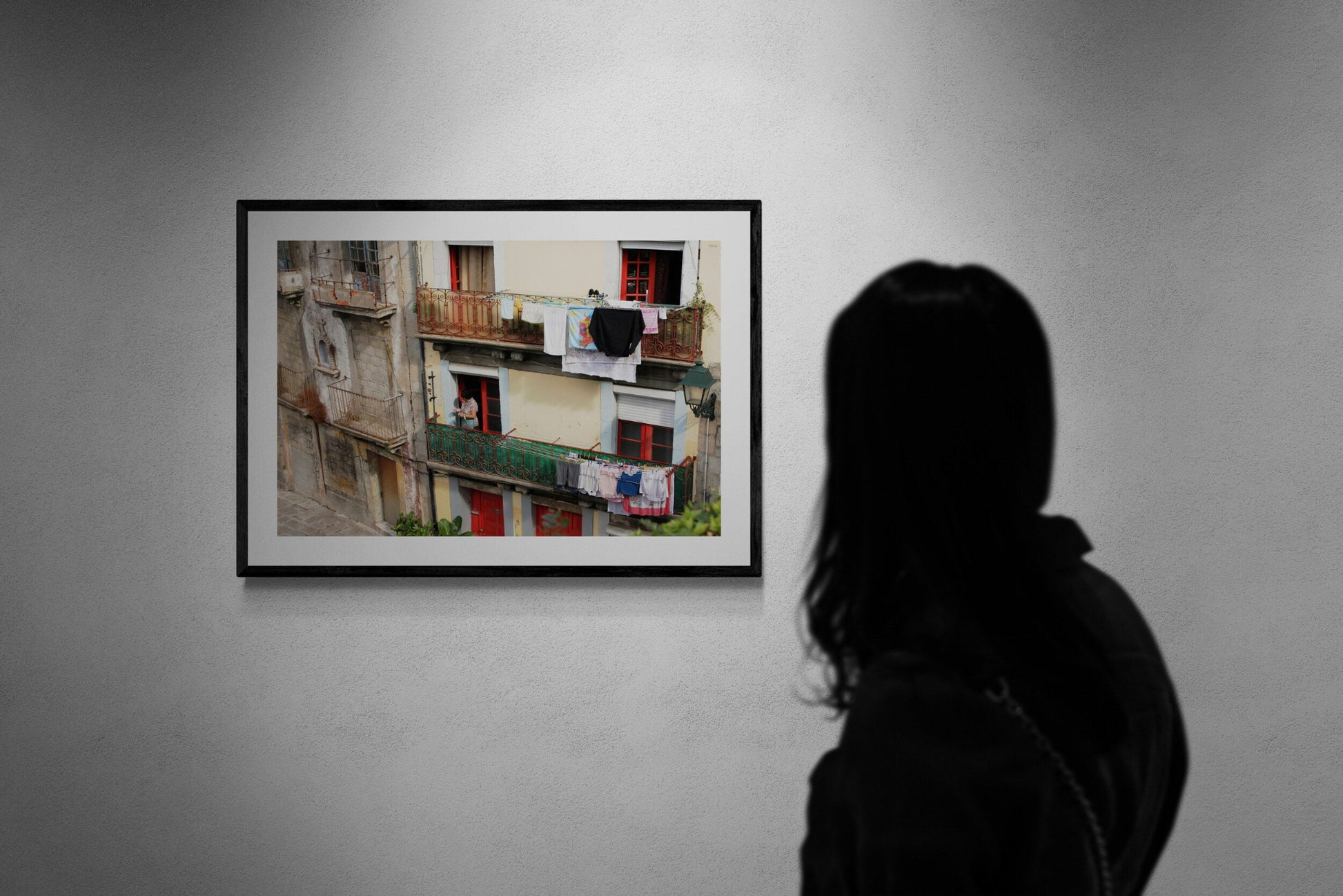 Person viewing a framed photograph of a street scene on a wall. Portuguese Woman Hanging Laundry, Original Photograph by Kim A. Bailey