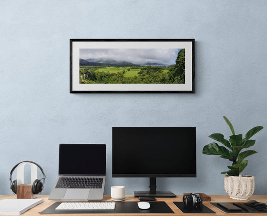 Modern office desk setup with a laptop, monitor, and plant against a light blue wall.Princeville Panoramic, Kauai Hawaii, Original Photograph by Kim A. Bailey