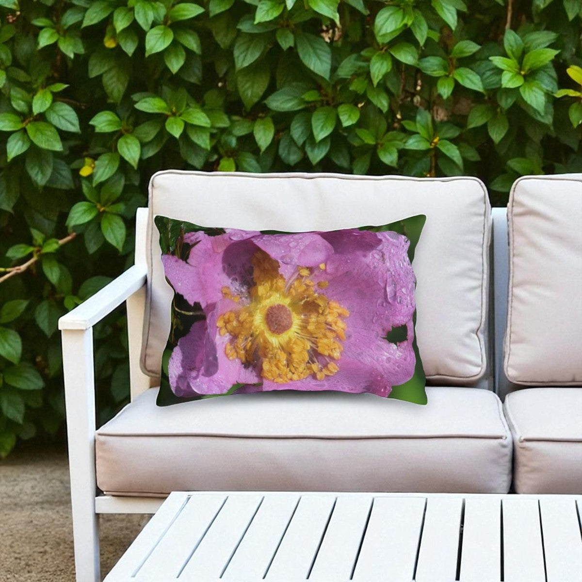 Floral pillow on a white outdoor sofa with green foliage in the background