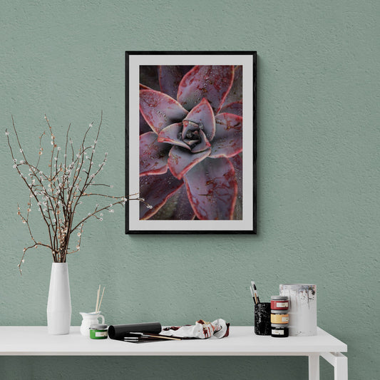 Framed succulent art print on a green wall above a white table with stationery items.