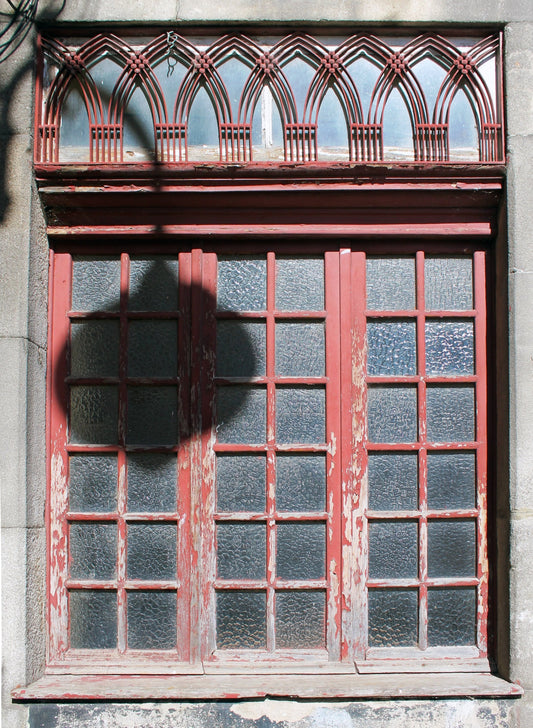 An old window painted red with multiple small rectangular glass panes and a shadow of a street lamp cast across it, against a gray background. Red Window - Portugal, Original Photograph by Kim A. Bailey