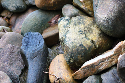 A close-up photograph of variously colored river stones, including blues, greens, yellows, reds, and grays, organically arranged and peaking above water.