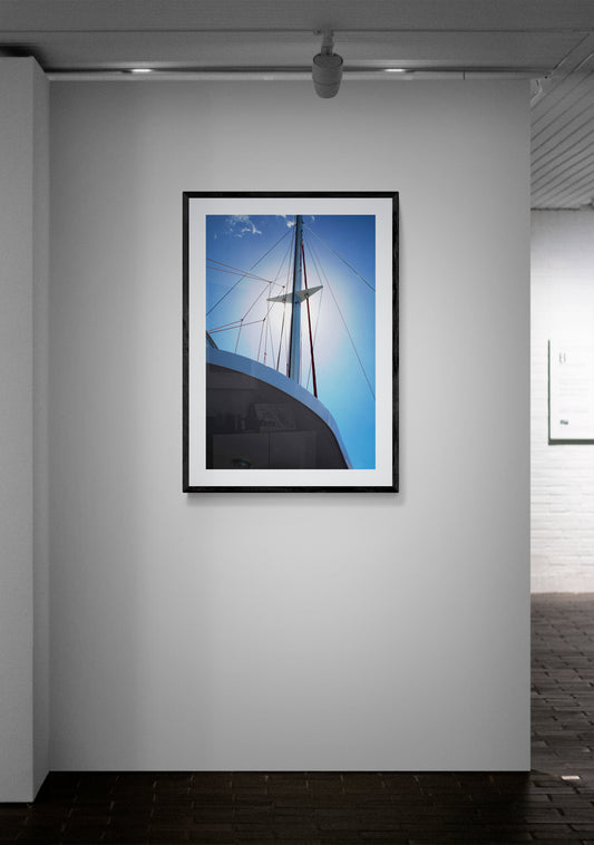 Framed photograph of a sailboat against a blue sky on a gray wall.