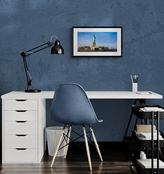 Modern office setup with a desk, chair, lamp, and framed picture on a blue wall.