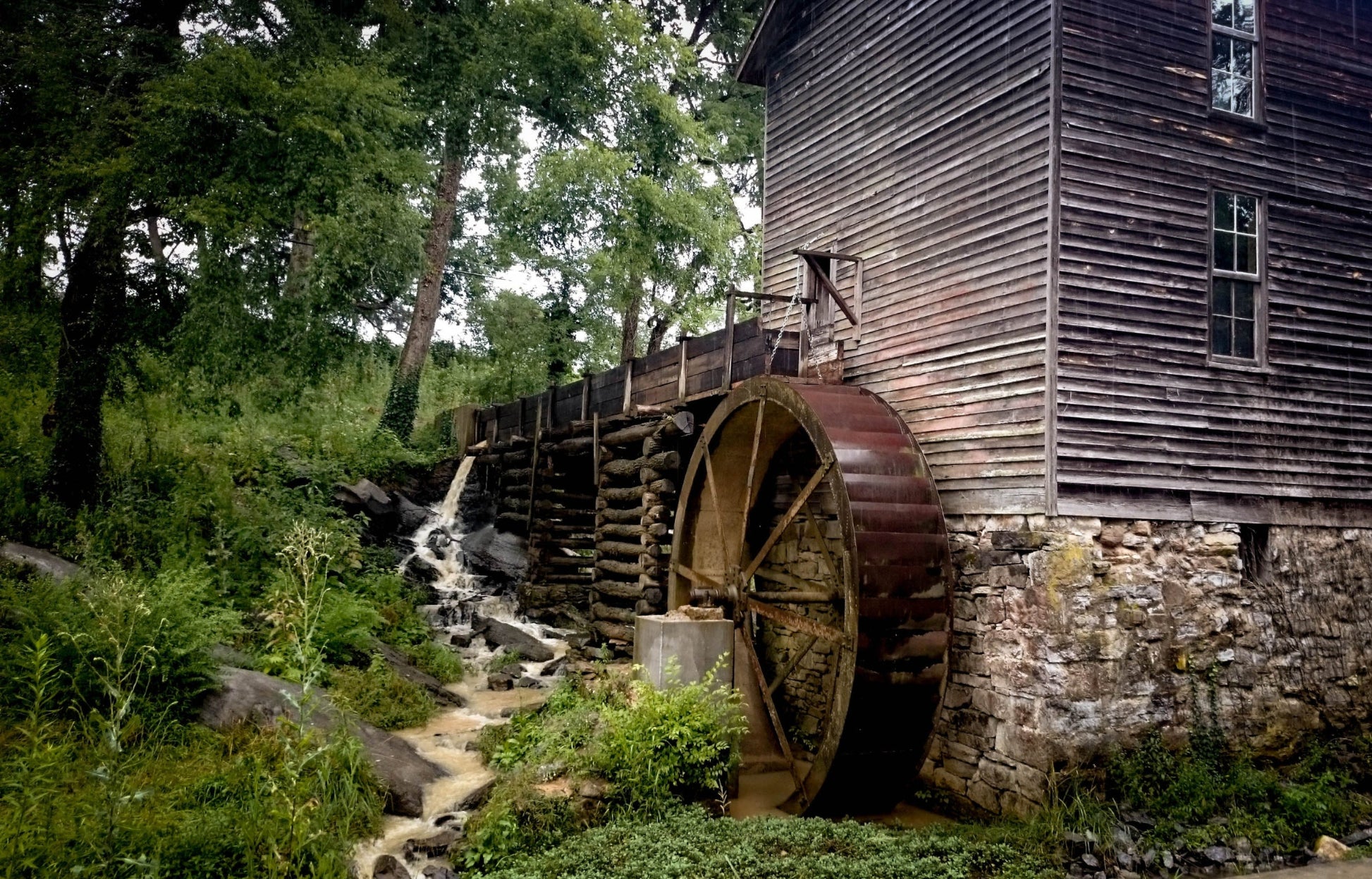 A photograph of a rustic watermill in Tennessee with a wooden wheel and a weathered exterior, surrounded by greenery. Tennessee Watermill, Original Photograph by Kim A. Bailey