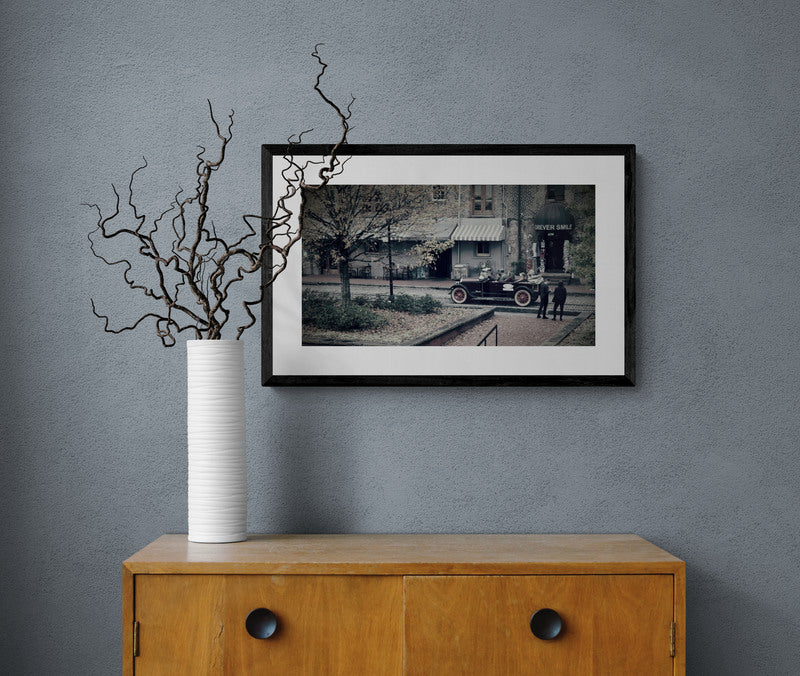 Framed black and white photo on a gray wall above a wooden cabinet with a vase and branches.