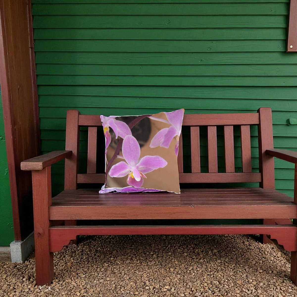 Wooden bench with a decorative pillow featuring pink flowers against a green wall.