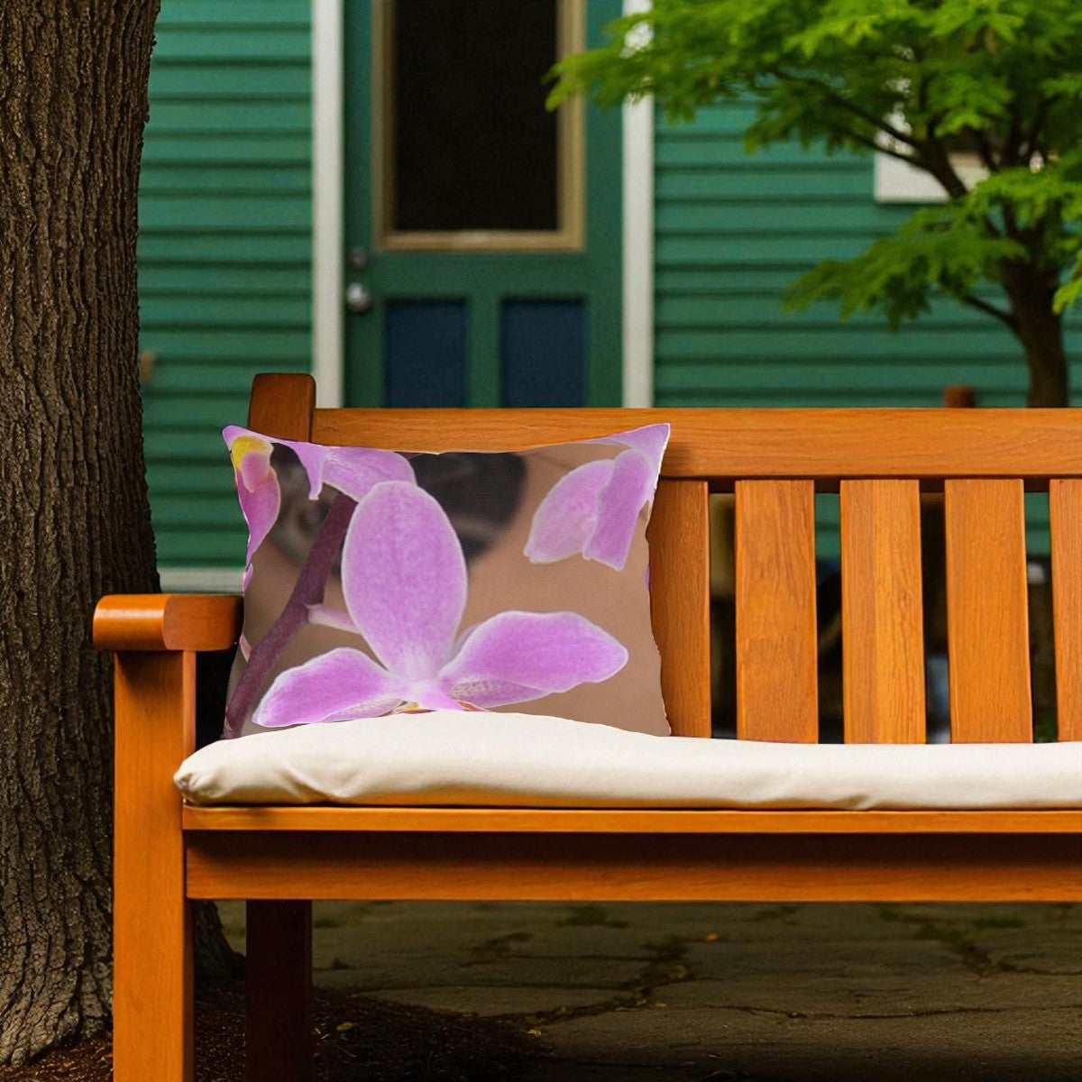 Wooden bench with a decorative pillow featuring purple flowers, set against a green house and tree background.
