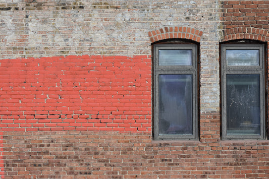 Photograph of two arched windows set in a red-striped brick wall, with a clear blue sky visible through the windows.