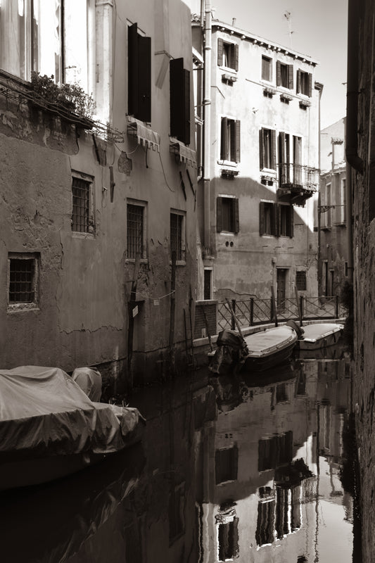 A sepia-toned photograph of a quiet canal in Venice, Italy, with historic buildings on either side and a boat partially visible.