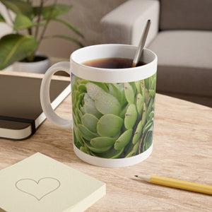 Mug with green plant design on a wooden table with a notebook and pen.