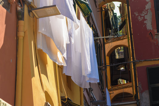 Photograph of white linens hanging out to dry with a view of buildings in the background, capturing a serene Italian atmosphere. White Linens, Original Photograph by Kim A. Bailey