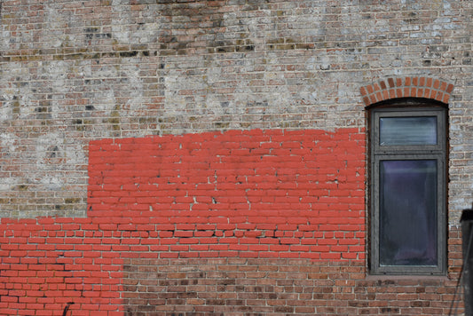 A color photograph featuring a striped red and orange brick wall with an arched window in the center, set against a gray brick background. Window in Brick Wall, Colorado