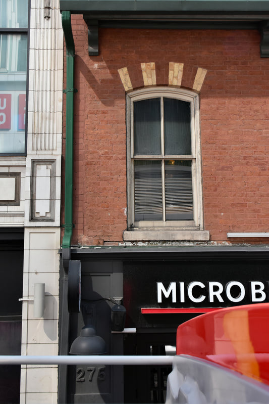 A brick building facade with a single arched window above a storefront sign reading MICRO B, shown in an urban street setting.